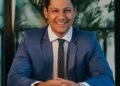 A smiling businessman in a blue suit at his desk, Positive Phil