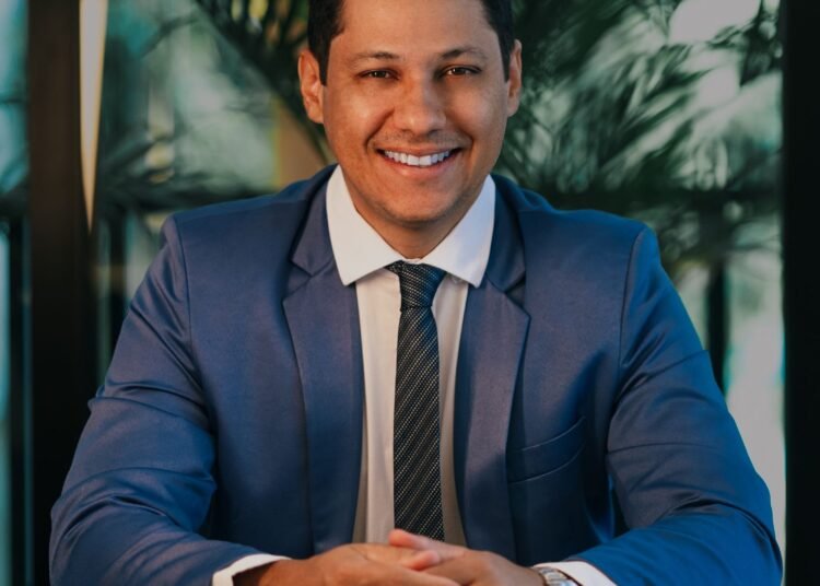 A smiling businessman in a blue suit at his desk, Positive Phil