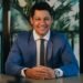 A smiling businessman in a blue suit at his desk, Positive Phil