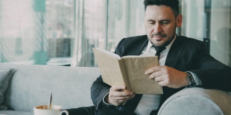 A man in a suit reading a book in a cafe, Positive Phil