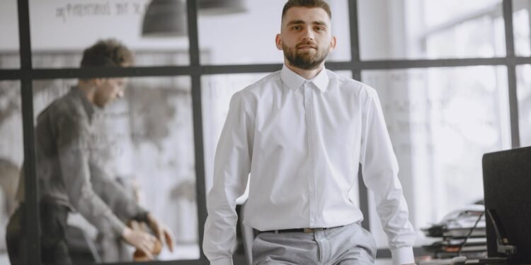 A confident man in a white shirt leaning on a desk, Positive Phil