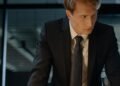 A professional man in a suit leaning over a desk, Positive Phil