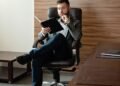 A man in a suit reading in a stylish office, Positive Phil
