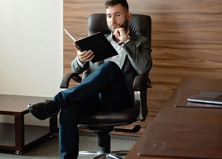 A man in a suit reading in a stylish office, Positive Phil