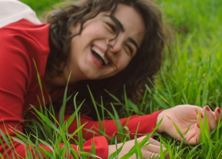 A woman in a red shirt smiling in the grass, Positive Phil