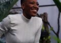 A smiling woman in a white sweater among green plants, Positive Phil