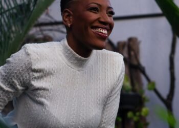 A smiling woman in a white sweater among green plants, Positive Phil
