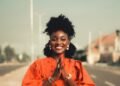 A woman in an orange outfit smiling on a city street, Positive Phil