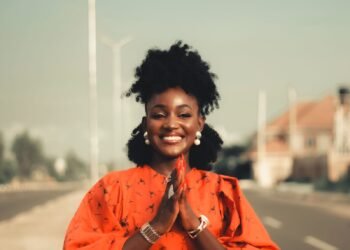 A woman in an orange outfit smiling on a city street, Positive Phil