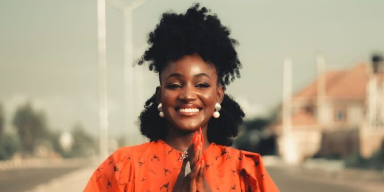 A woman in an orange outfit smiling on a city street, Positive Phil