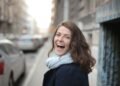 A woman in a scarf smiling on a city street, Positive Phil