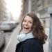 A woman in a scarf smiling on a city street, Positive Phil