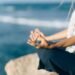 Hands resting in a meditation pose by the ocean