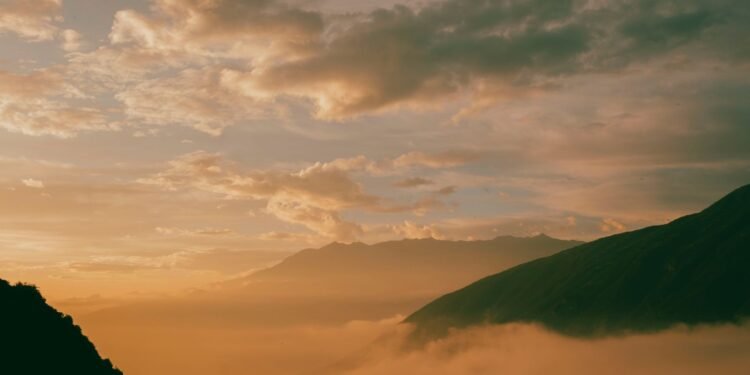 Golden sunrise glowing through low clouds over misty hills