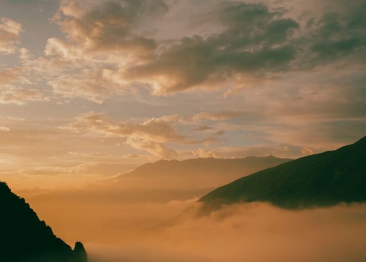 Golden sunrise glowing through low clouds over misty hills