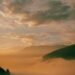 Golden sunrise glowing through low clouds over misty hills