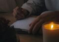 Person writing in a journal by candlelight