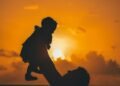 silhouette photo of man carrying baby during golden hour