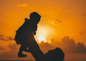 silhouette photo of man carrying baby during golden hour